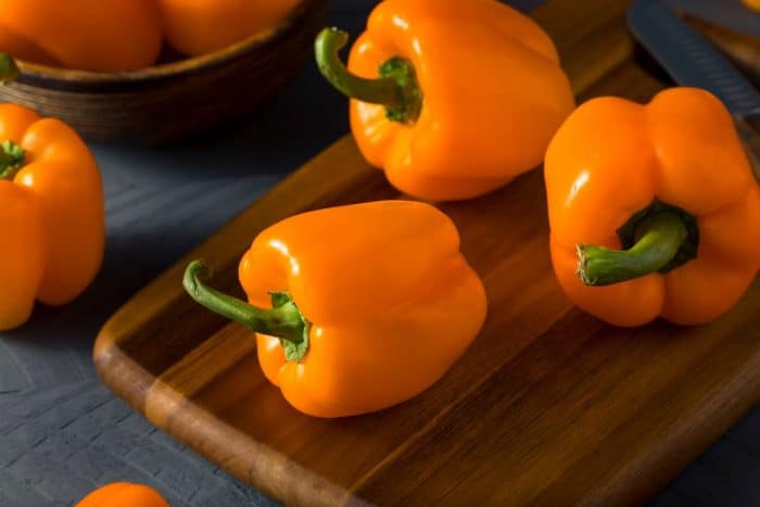 Raw Organic Orange Bell Peppers placed on a wooden chopping board