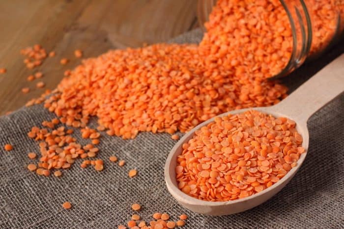 Refined red lentils in wooden spoon and glass jar on linen sackcloth