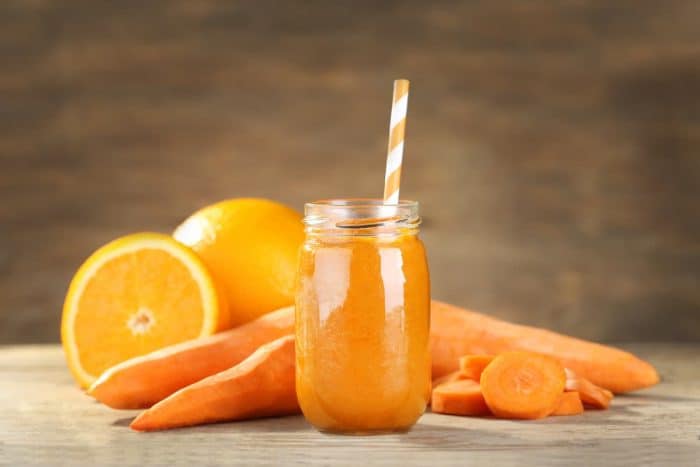 Jar with carrot and orange smoothie on wooden table with fresh carrots and oranges on the background
