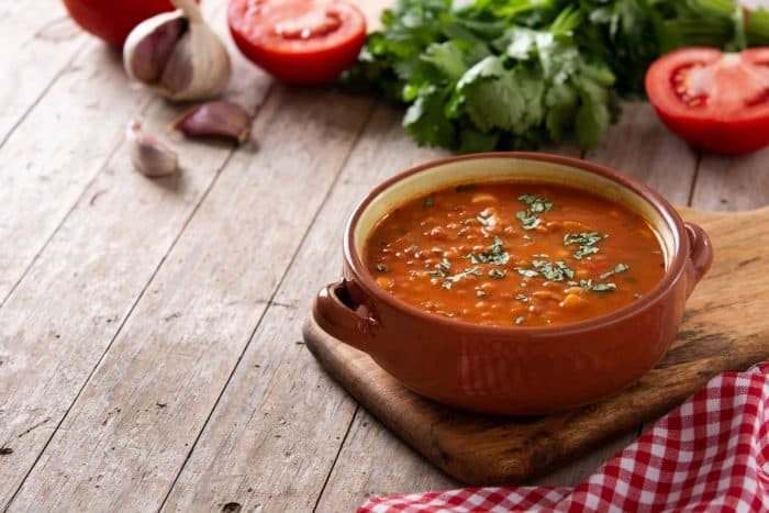 a bowl with freshly cooked red lentil soup topped with green herbs with fresh ingredients on the background
