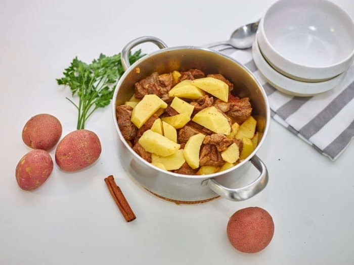 Add the marinated beef to a Dutch oven or stock pot over medium heat, making sure to include all its juices and seasonings. Add chopped potatoes to the pot with the beef.