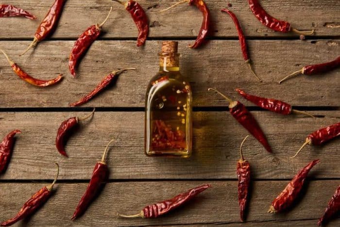 Top view of bottle with flavored oil and red hot chili peppers on wooden background