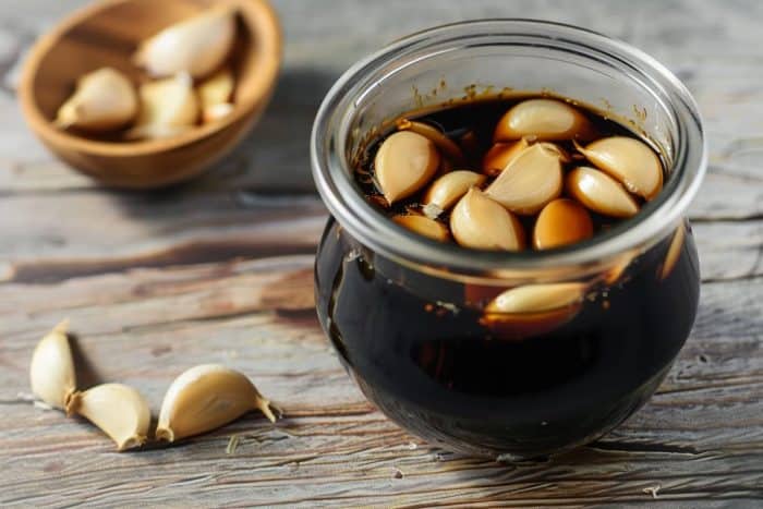 realistic image of peeled garlic marinated in soy sauce placed on a wooden table