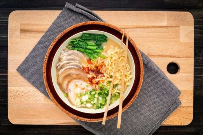 Asian ramen noodle pork bone based soup with pork chashu on cutting board background.