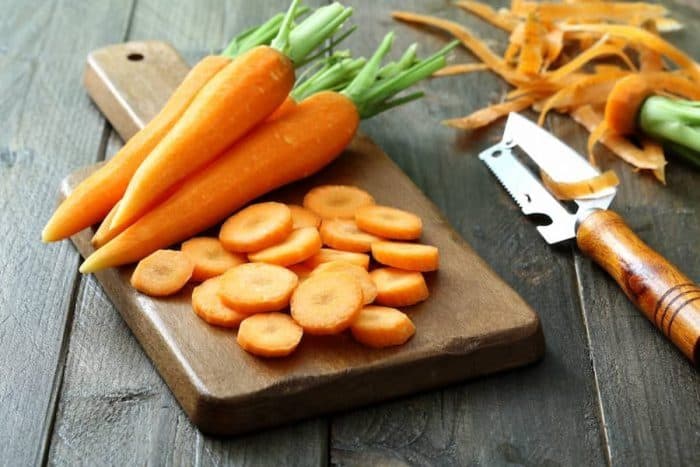 whole and sliced fresh carrots placed on a wooden chopping board