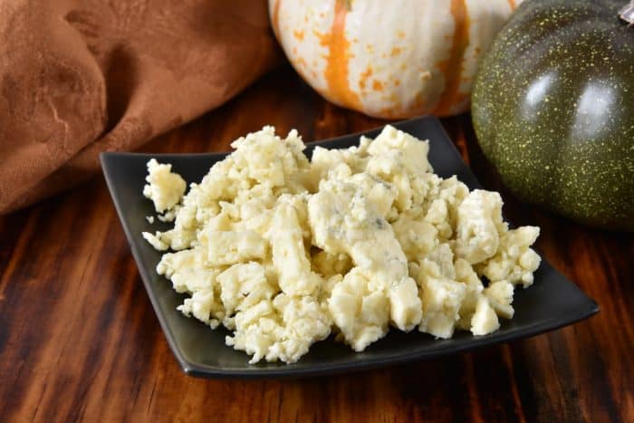 A small dish of blue cheese crumbles on a cutting board.