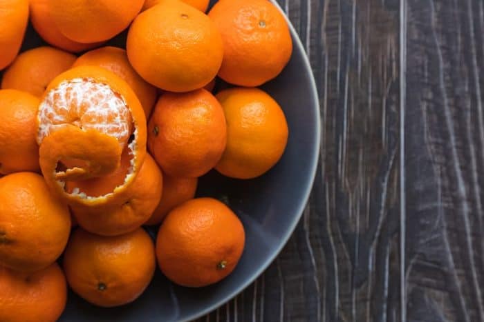 A bowl of ripe orange tangerines on a wooden table shot from above