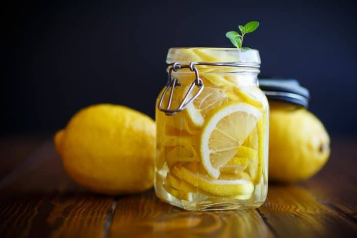 a jar of Pickled lemons in sugar syrup on a wooden table with fresh lemons on the background