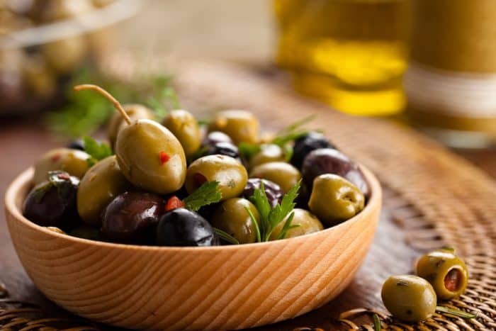 a wooden bowl full of spanish marinated olives placed on a wooden table