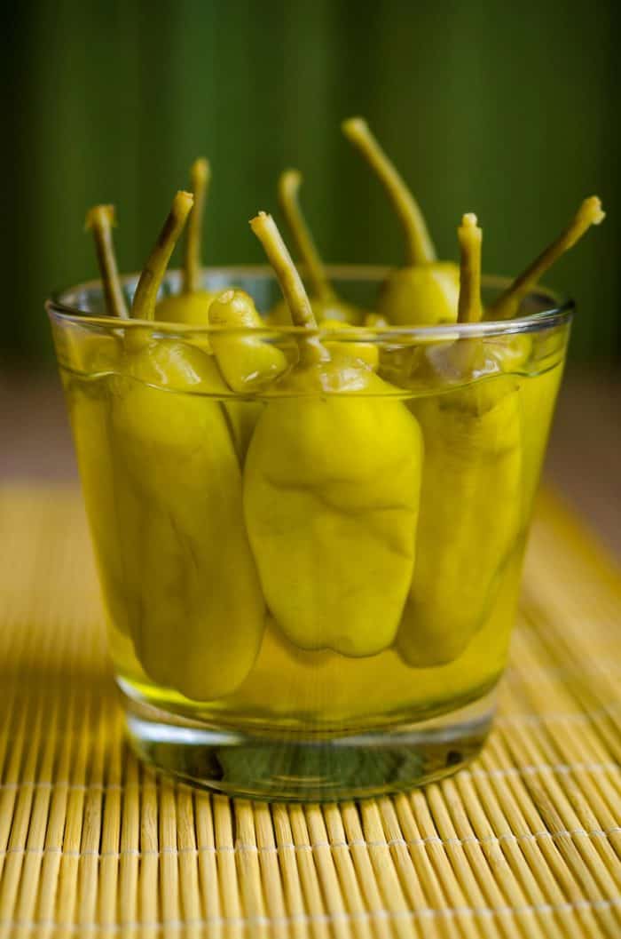a small jar full of Pepperoncini placed on a wooden table