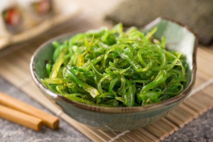 s small bowl full of wakame seaweed with choopstick on the background