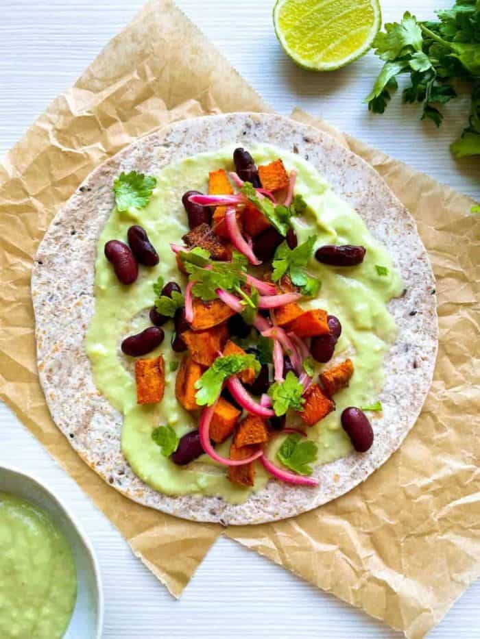 Spread a dollop of the avocado sauce over each tortilla and top with roasted sweet potatoes, red beans, pickled red onion, and fresh parsley. 