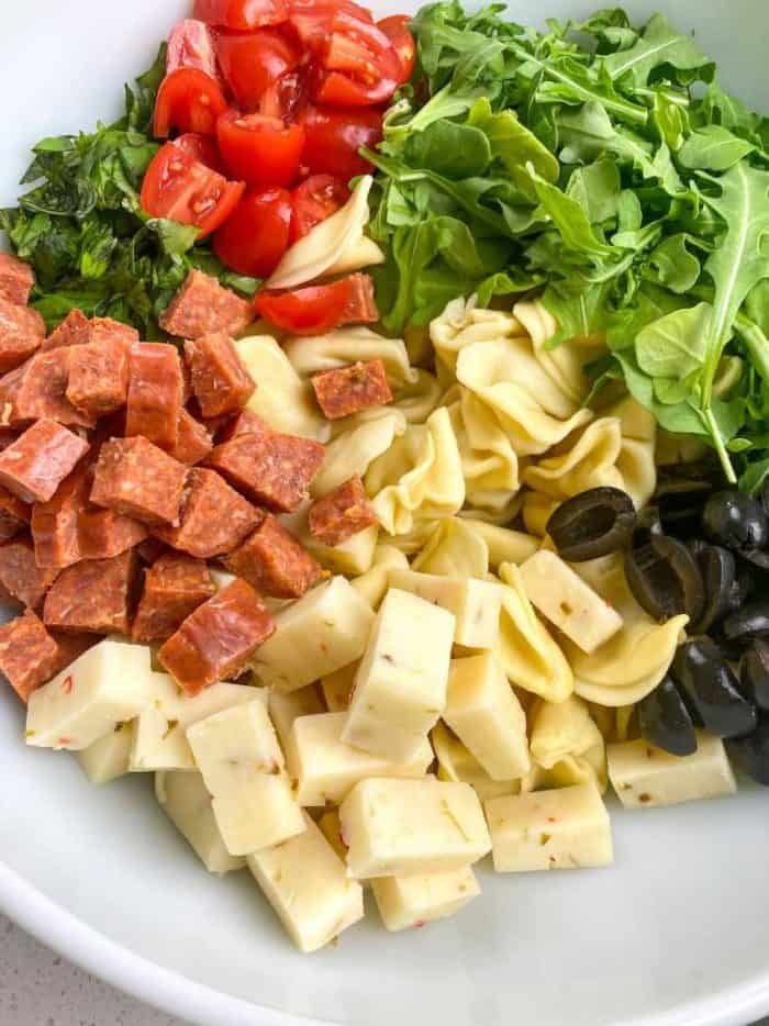 Transfer the cooled tortellini to a large mixing bowl. Add fresh arugula, thinly sliced basil, chunks of pepper jack cheese, small pieces of pepperoni, halved black olives, and halved cherry or grape tomatoes