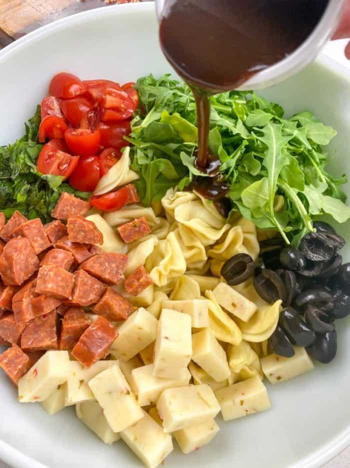 Pour half of the balsamic vinaigrette over the salad ingredients and gently fold everything together with a spoon or salad tongs, ensuring that the tortellini and add-ins are evenly coated with the dressing.