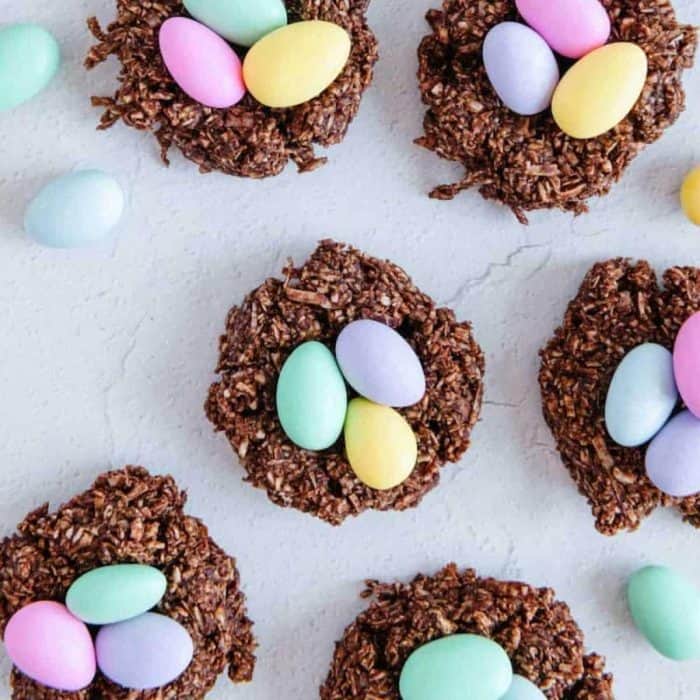 They feature a crunchy coconut and chocolate base with a nest-like appearance, cradling mini pastel-colored chocolate eggs for a playful nod to the holiday.