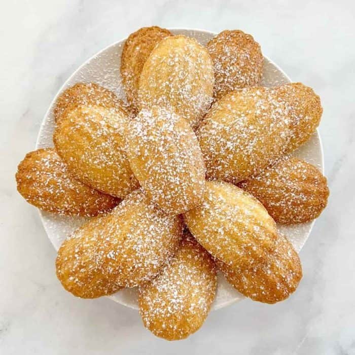 These dainty vegan madeleines feature a tender crumb with a luscious, buttery texture, crowned by a golden crust. A hint of lemon zest weaves through each bite, providing a delicate, fragrant note.