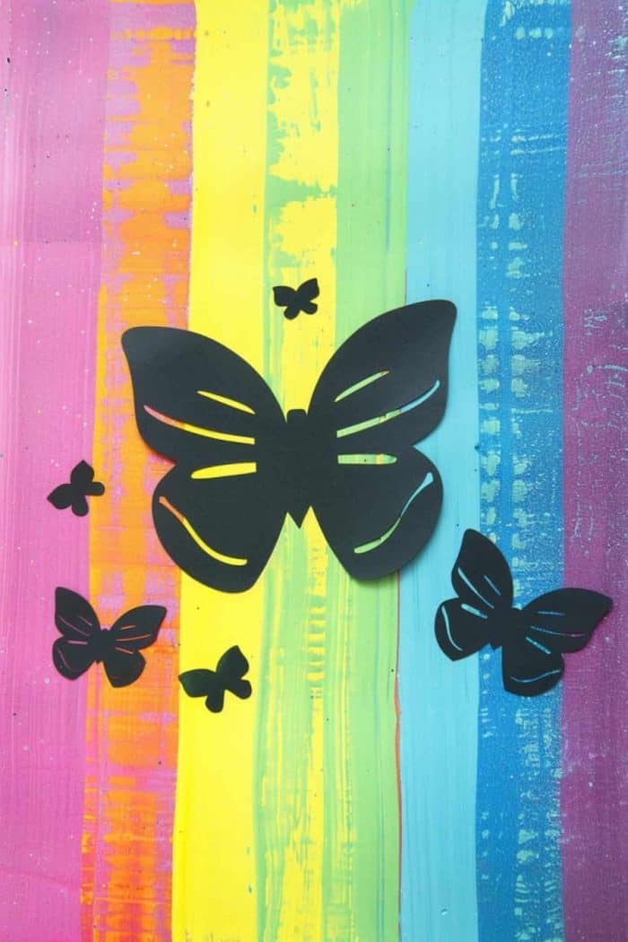 Paper silhouettes of butterflies and hearts against a painted rainbow backdrop create a striking piece of art that any young artist can make!