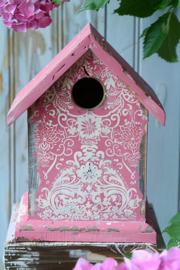 With intricate lace patterns on a soft pink base, this painted birdhouse idea exudes delicate femininity and grace. It’s perfect to use in a flower garden teeming with different blooms.