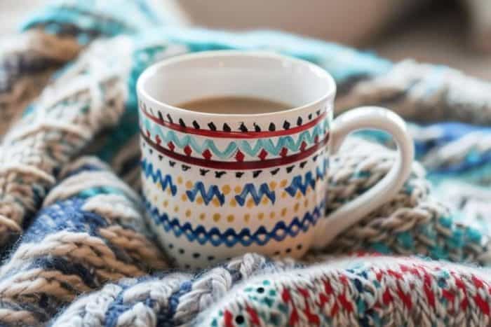 The surface of this mug is painted to resemble the comforting texture of a knitted sweater, complete with interlocking stitches and a pattern that invites one to wrap their hands around it as if warming up by the fire.