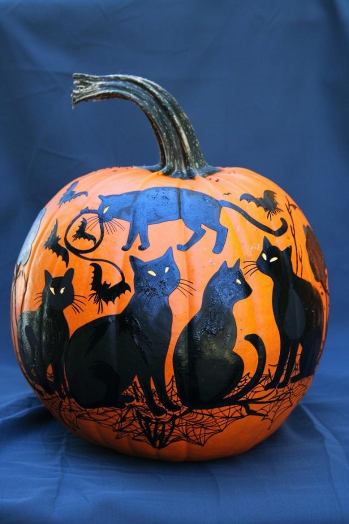 Silhouettes of black cats in various poses encircle the pumpkin, set against a deep midnight blue background. 