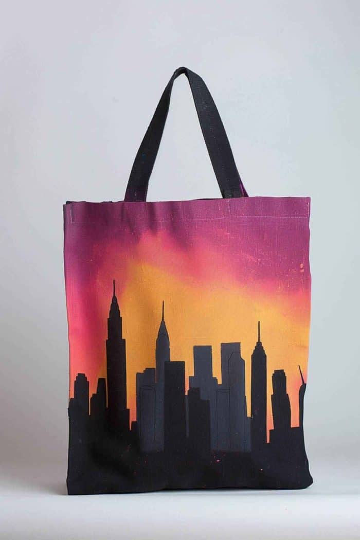 The city skyline is rendered in a monochromatic scheme, capturing the silhouettes of skyscrapers as they stand tall against the soft gradients of a dawn sky on the canvas tote.