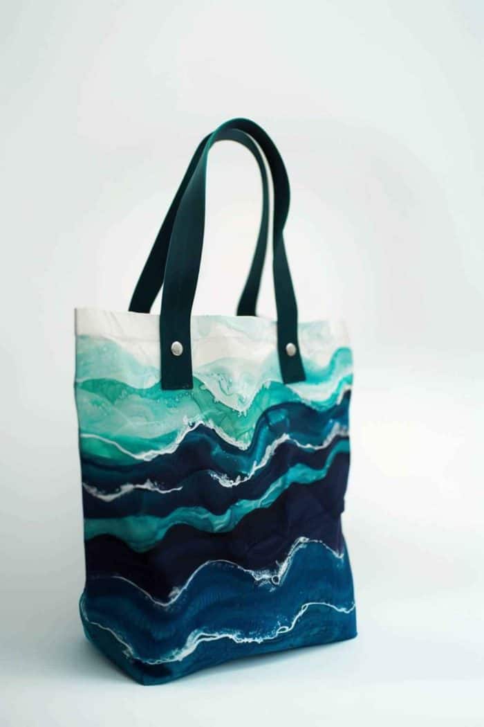 Capturing the essence of the ocean's tranquility, the tote features painted waves in a gradient of blues and greens, with white frothy tips that give a sense of movement.