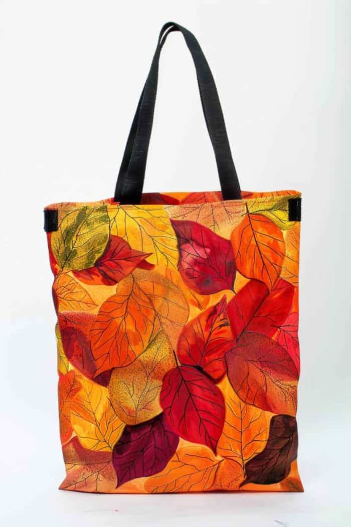 A cascade of autumn leaves, in rich oranges, reds, and yellows, adorns the tote. Some leaves overlap, others solitary, as if caught mid-tumble by a gust of wind.