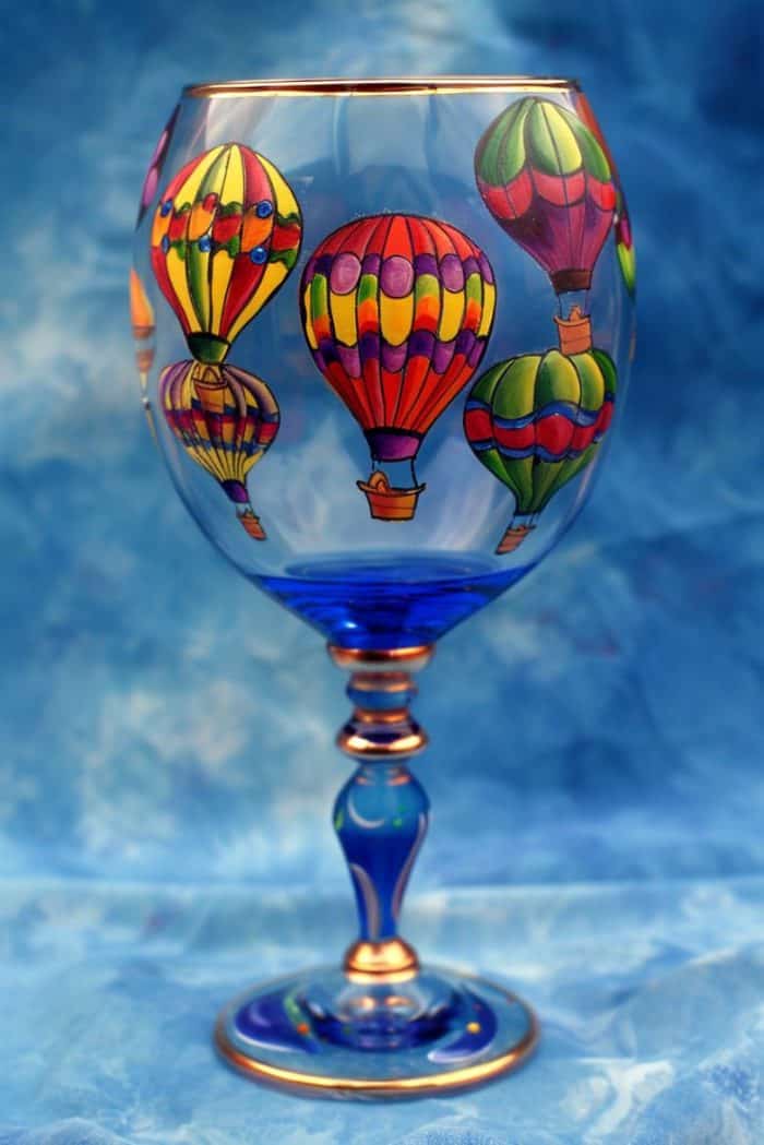 Brightly colored hot air balloons, complete with intricate patterns and glistening reflections, float across the glass against a sky blue backdrop. 