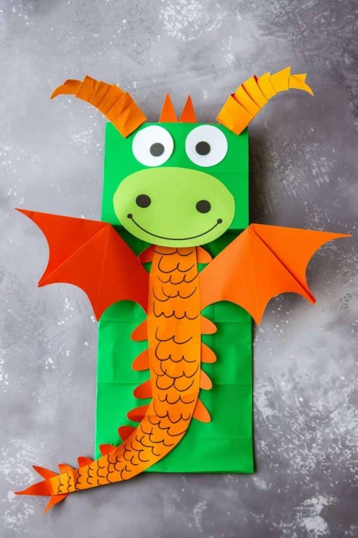 Adventure awaits with this dragon made of a green paper bag! For an extra magical look, it sports orange ears, orange wings, and black scales.
