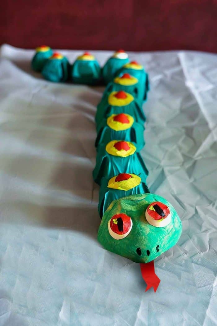 Assemble a snake by connecting a series of egg carton cups, painting the exterior with alternating colors to create a patterned effect. 