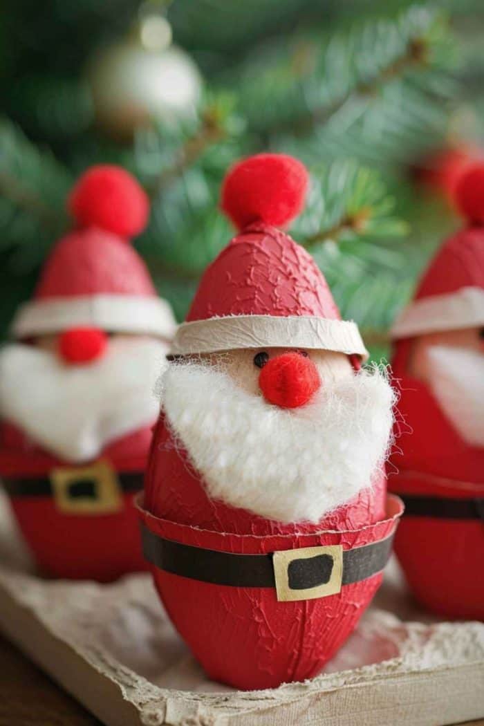 Use egg carton cups as the base for Santa figures, painting them red and adding details like belts. Glue on fluffy cotton for beards and small red pom-poms for noses, finishing with a crafted hat on top.