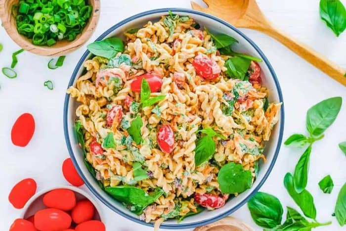 Gluten-free pasta twirls are tossed with juicy tomatoes and a medley of colorful peppers, all brought together by a creamy, tangy dressing with freshly picked tomatoes and basil scattered on the sides