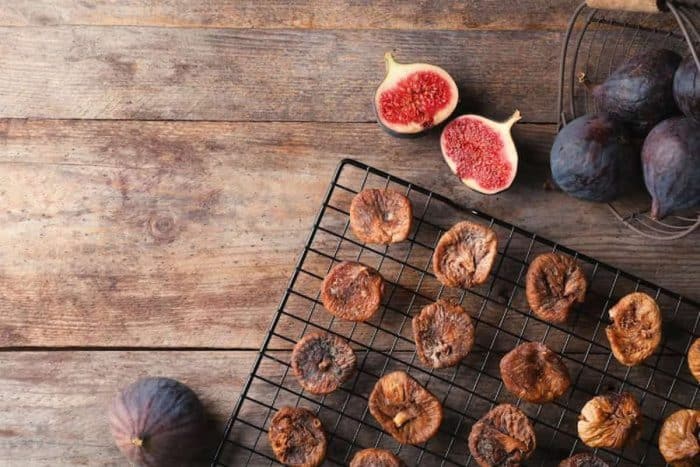 dry figs are placed in a rack for cooling with fresh figs beside it on a wooden table