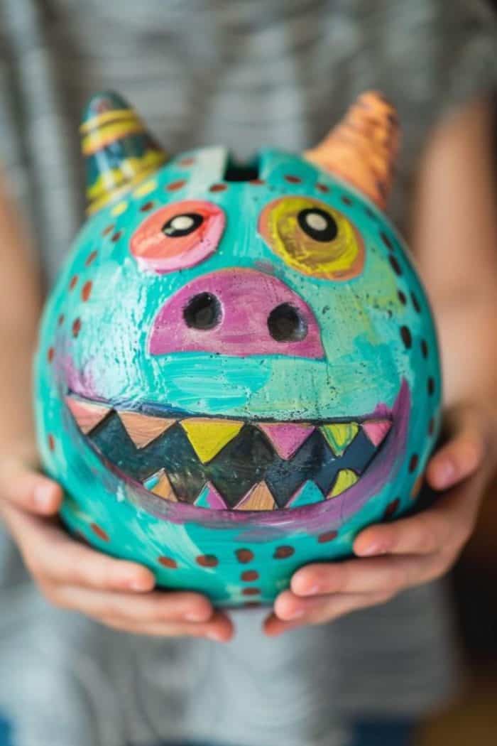This piggy bank features a friendly monster face with a wide grin and big eyes painted in vibrant colors.