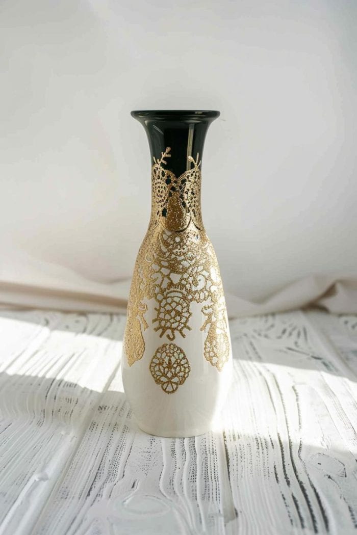 A pattern of intricate lace is wrapped around the vase before it is spray-painted with a light color, leaving the lace's detailed pattern etched into the surface. 