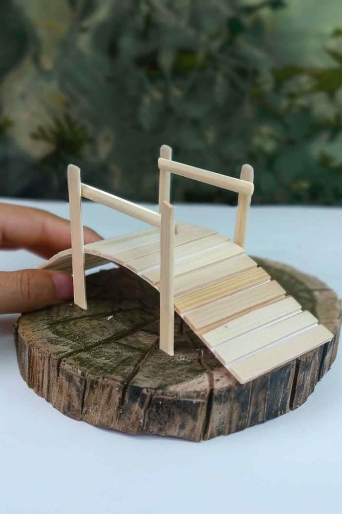 Build miniature bridges with popsicle sticks. Cut the sticks to remove the rounded ends, glue them on paper to form the base, and add details like railings. 