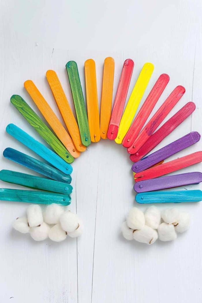 Create an artisanal rainbow using popsicle sticks. Paint each stick in a different color of the rainbow and arrange them in an arc shape. Glue the sticks onto a piece of cardboard or thick paper, adding cotton ball clouds at each end.