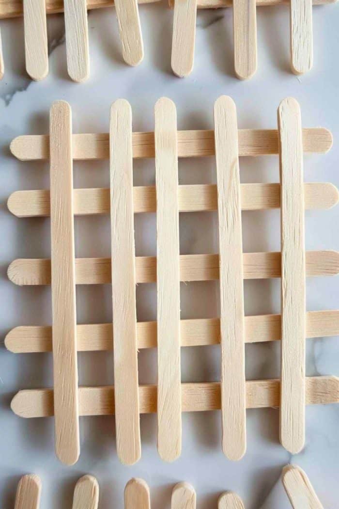 Using popsicle sticks, create coasters by arranging the sticks in a grid pattern and gluing them together. These crafty coasters will protect surfaces while adding a playful touch to any table setting.