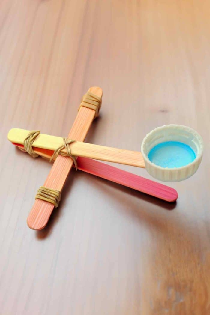 Build a popsicle stick catapult to introduce physics in a fun way. Stack and secure several sticks together with rubber bands to form the base, then create a lever arm using another stick and a bottle cap for the launching pad. 
