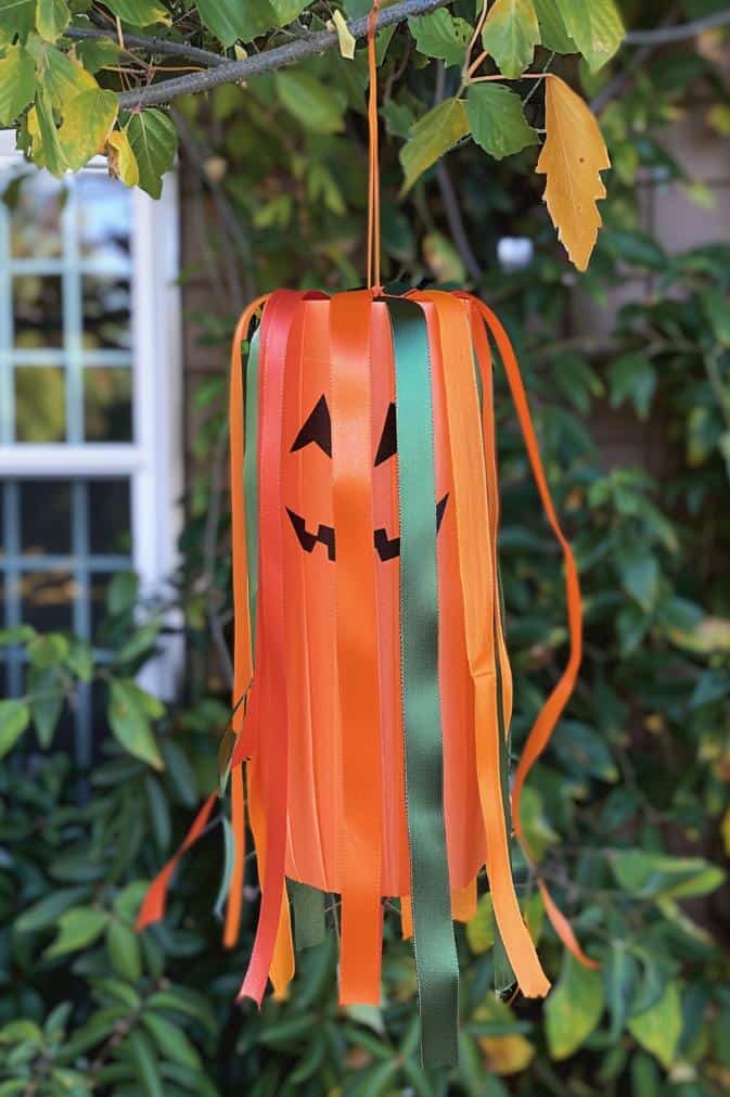 Make a pumpkin windsock by attaching strips of orange, yellow, and green ribbons to the bottom of a cylindrical orange base, which can be crafted from fabric or paper.