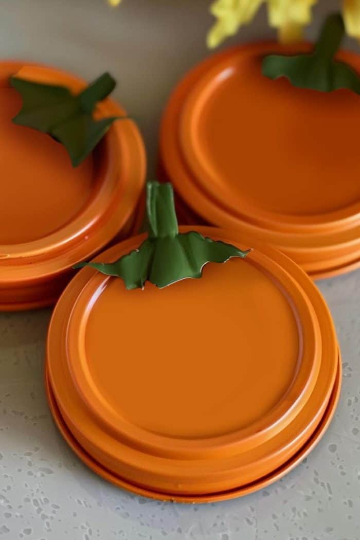 Transform jar lids into minimalist pumpkins by painting them orange and adding a green stem made with board paper.