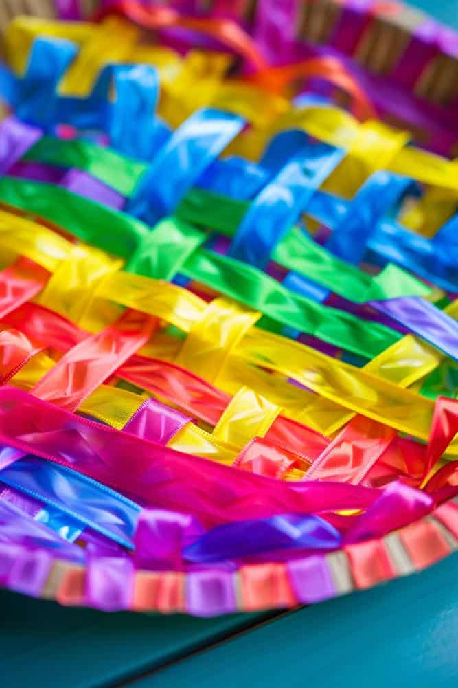 Create a woven masterpiece on a paper plate by interlacing strips of brightly colored ribbon or yarn through evenly spaced cuts along the plate's raised edge. 