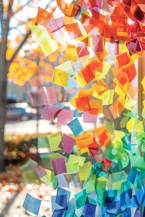 Assemble a stunning window decoration by gluing small squares of colored paper onto a clear adhesive sheet in a mosaic pattern. 