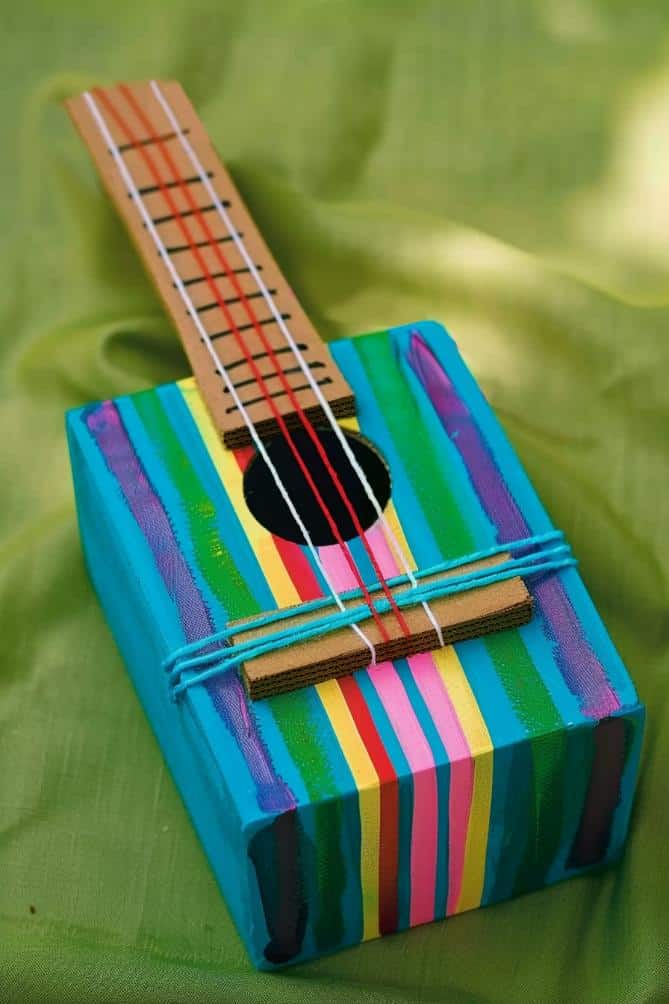 Convert an empty tissue box into a guitar by painting the body in soft rainbow stripes and stretching rubber bands of various thicknesses across the opening for strings. 