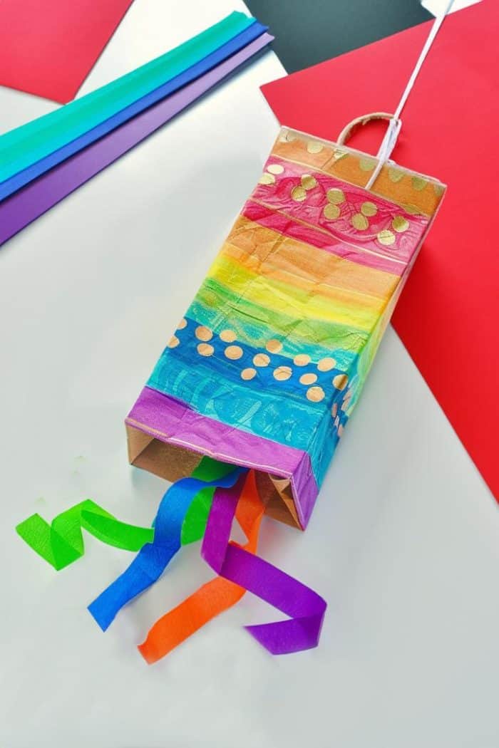 Create rainbow-colored stripes on a paper bag with markers to achieve a rainbow pattern, then attach paper streamers and a string for flying. 