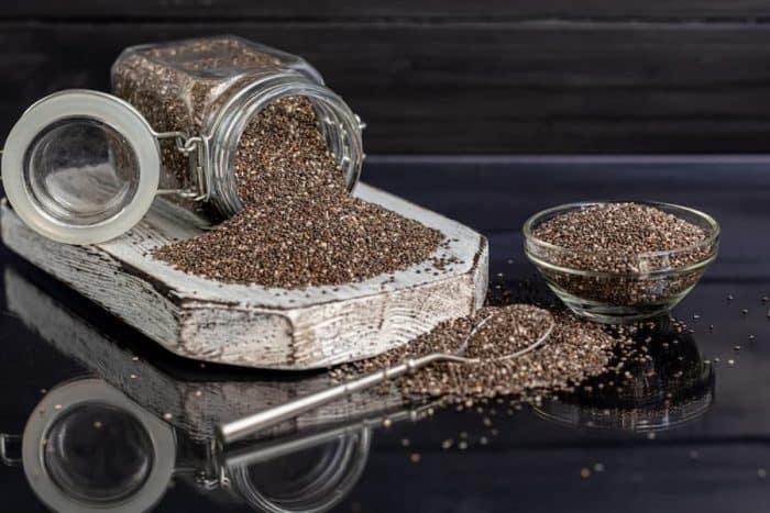 Black chia seeds in glassware contain healthy vitamins and minerals. On a black background with a metal spoon.