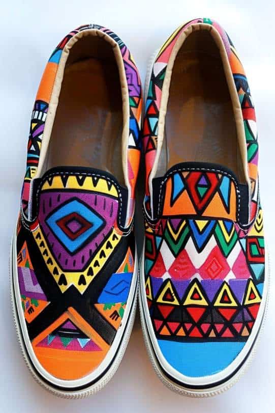 Canvas shoes are transformed into a tapestry of Aztec tradition with sharp geometric shapes like triangles and diamonds, rendered in a vivid color scheme. 