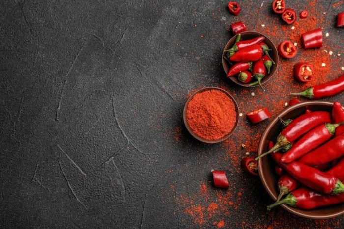 Flat lay composition with powdered and raw chili peppers on dark background