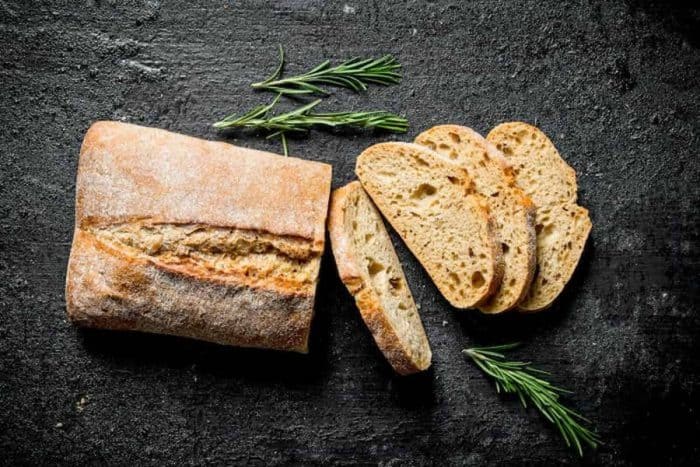 Sliced ciabatta bread with rosemary. On black rustic background