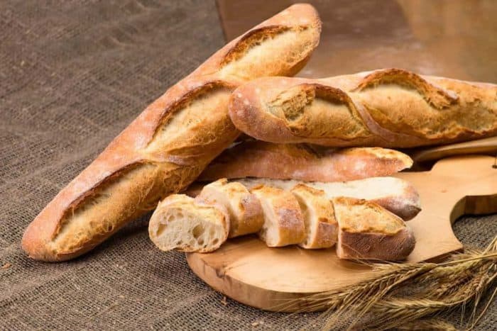 still life with French fresh bread baguettes with poolish on a wooden cutting board and wheat, shallow dof